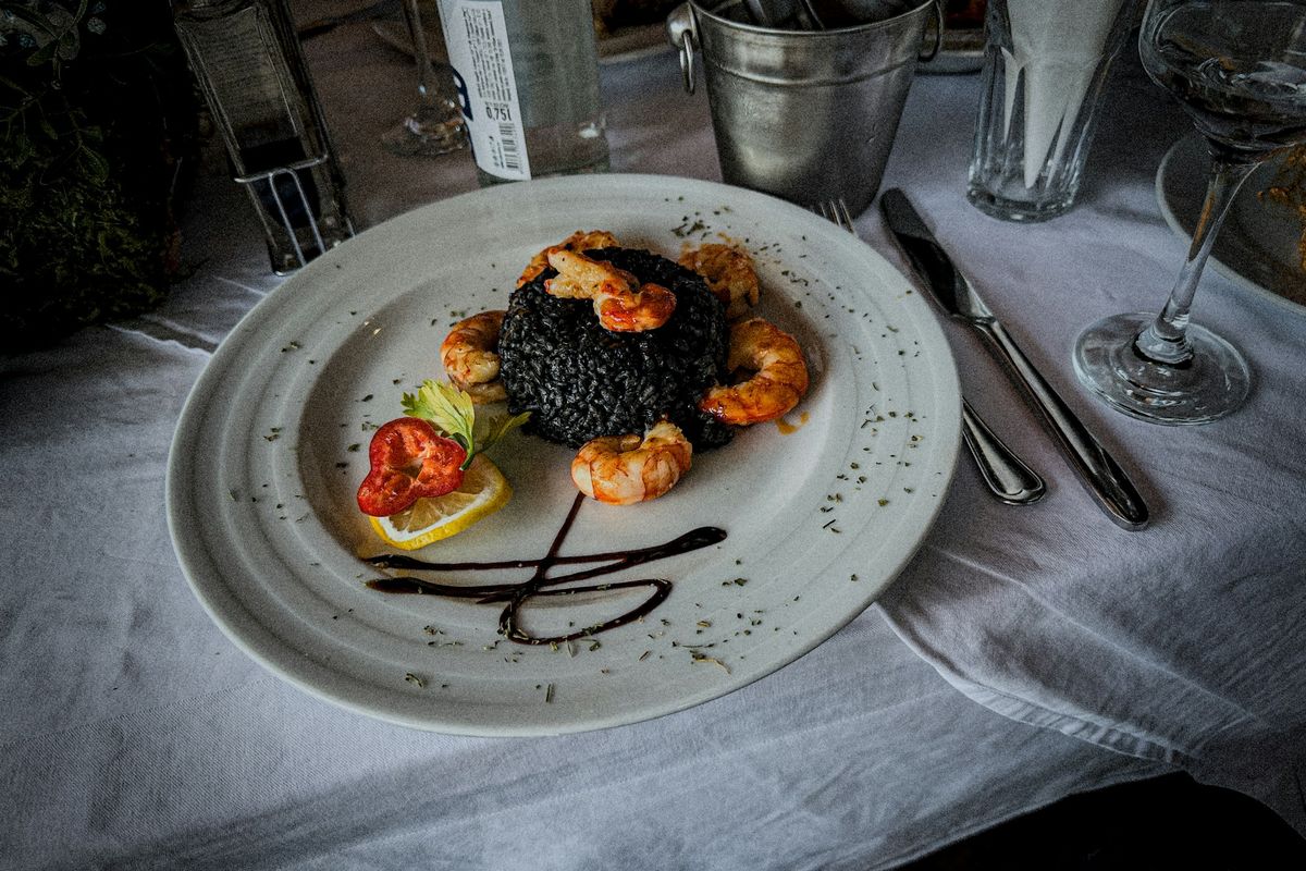 A plate of black cuttlefish-ink risotto with prawns on a restaurant table
