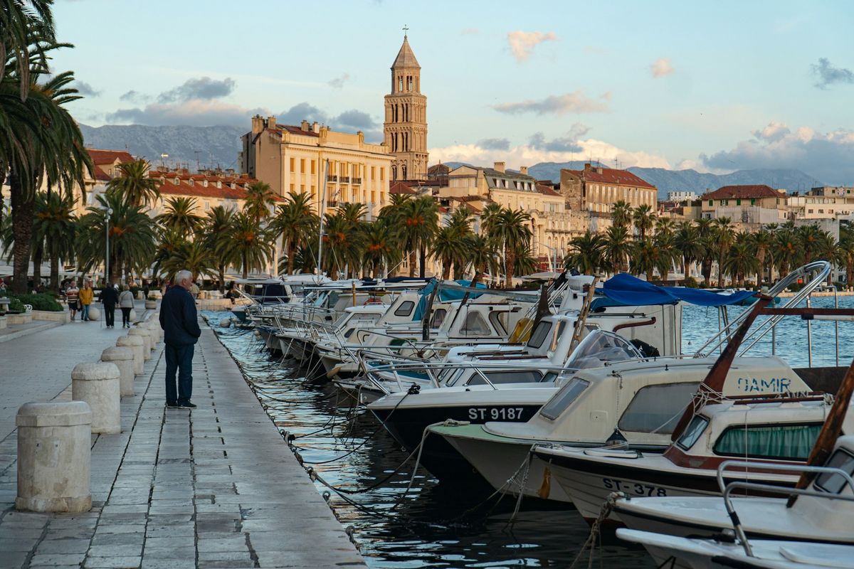 A man in a winter jacket on the quiet harbour wall in Split, with the cathedral bell tower behind