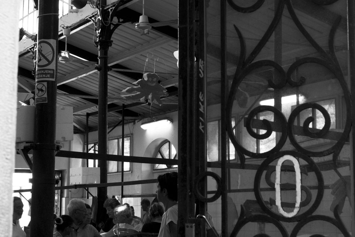 Shoppers inside Split's fish market hall, seen through its ornate iron gate